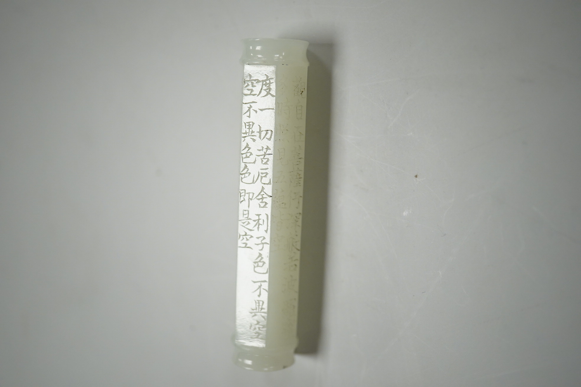 A Chinese pale celadon jade inscribed cylinder bead, 6.5cm long